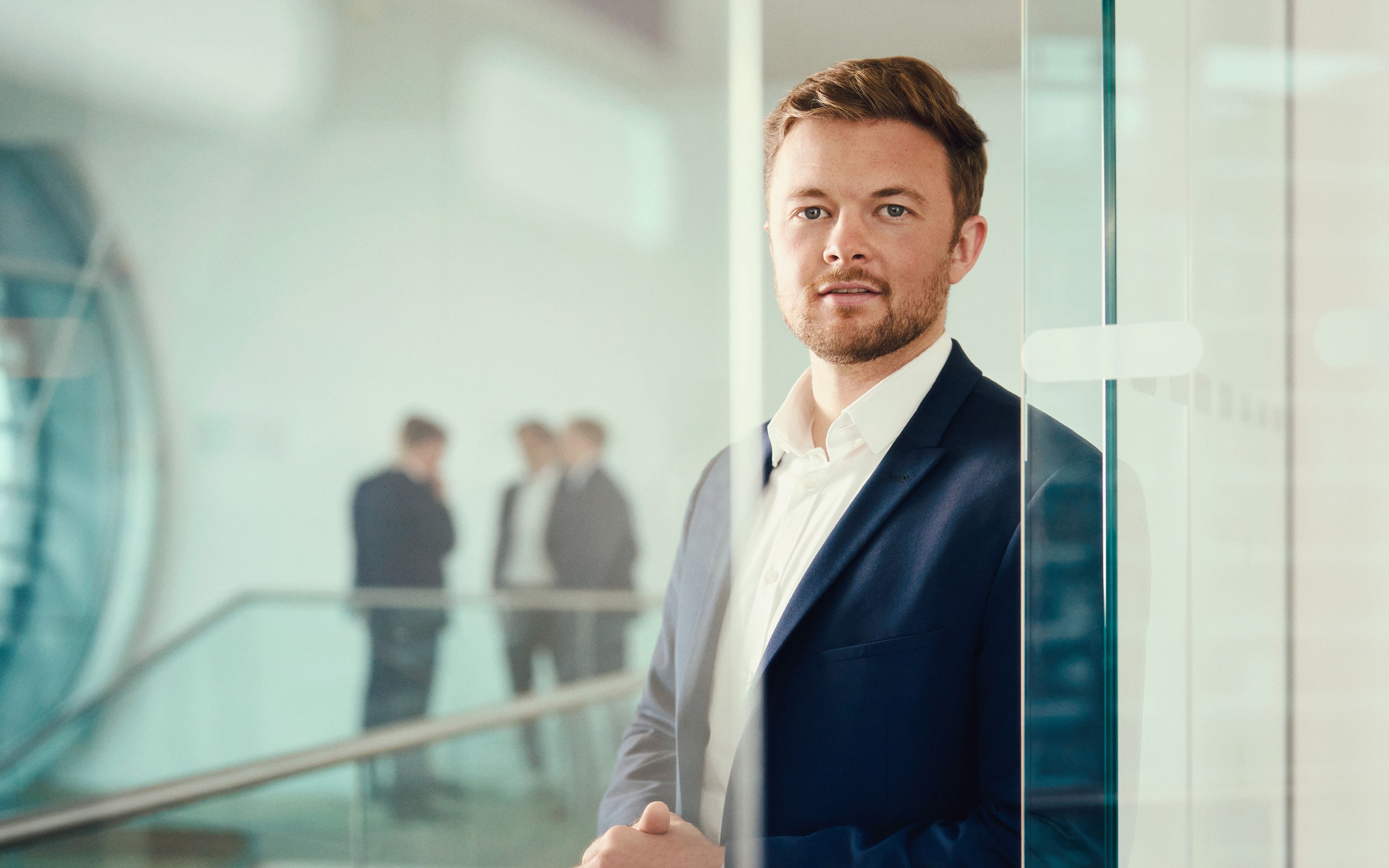 Portrait of an Aspera Partners consultant in a modern office, with a team conversing in the background.